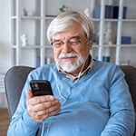 Older man with glasses looking down at mobile phone with earphones in
