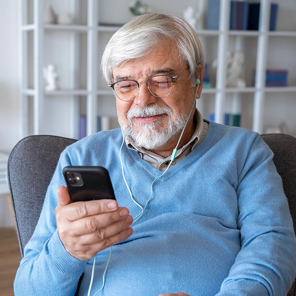 Older man with glasses looking down at mobile phone with earphones in